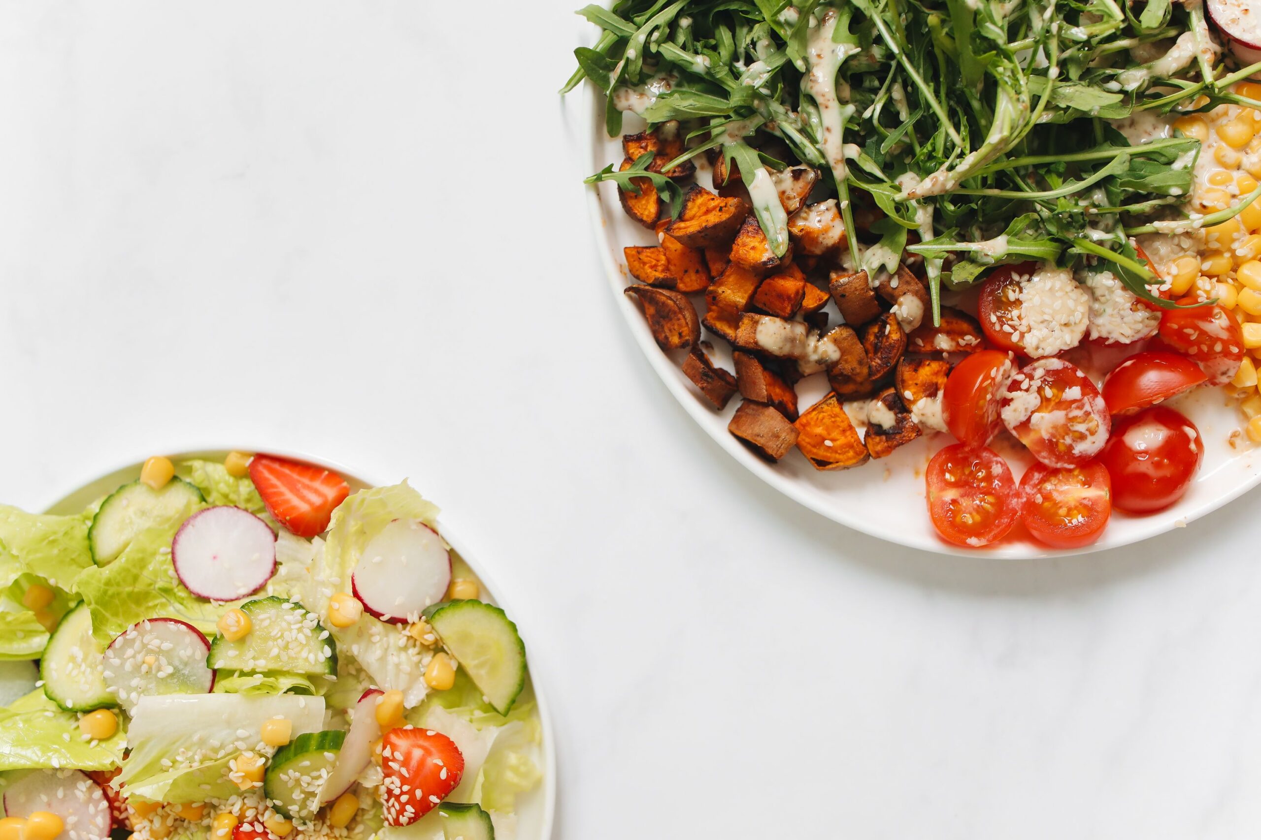 Vibrant fresh vegetable salads with mixed greens and toppings on a white surface.